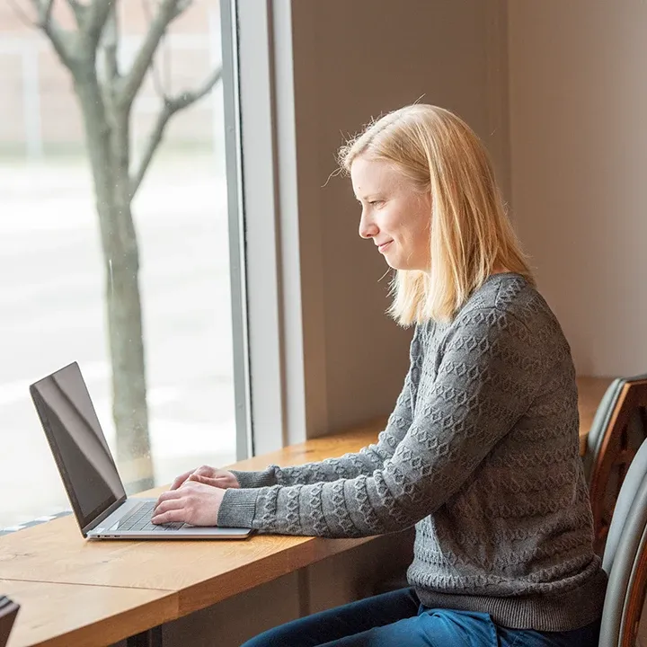 一个女人坐在靠窗的桌子前用笔记本电脑工作